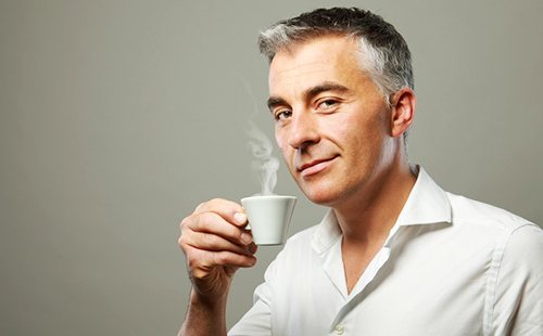 Седеющий мужчина с многозначительной улыбкой держит чашку